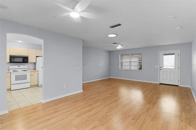 a view of empty room with wooden floor and kitchen view