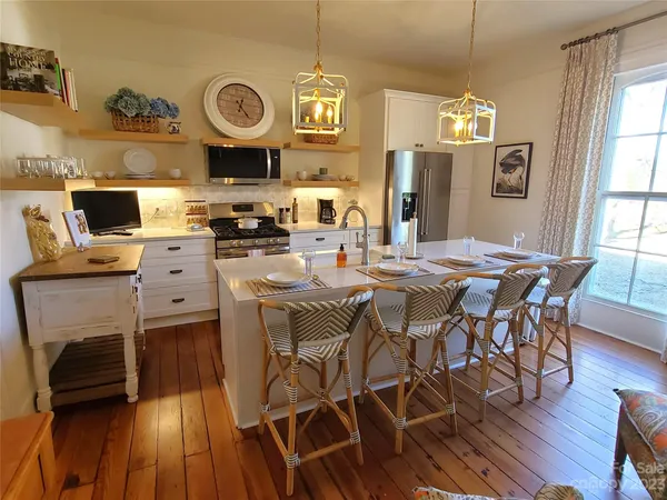 a large white kitchen with a stove a sink and a dining table with wooden floor