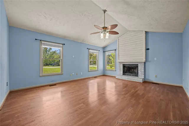 an empty room with windows fireplace and wooden floor