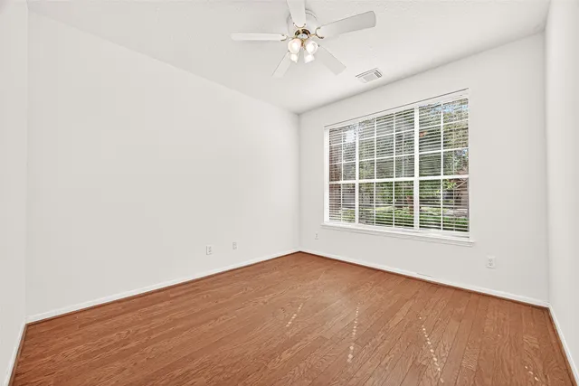 an empty room with wooden floor fan and windows