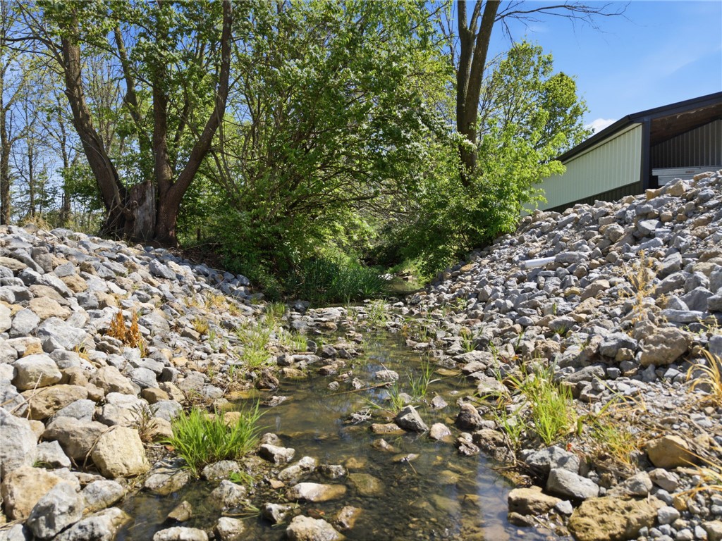 1602 Westboro Road Blanchester, OH 45107 - Photo 68 of 81 A tranquil creek flows through a rocky bed, bordered by lush trees and a glimpse of a structure.
