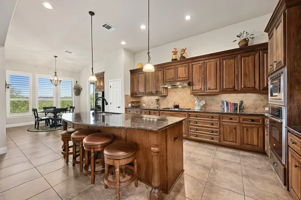 a kitchen with stainless steel appliances granite countertop wooden cabinets a stove a sink and a chairs