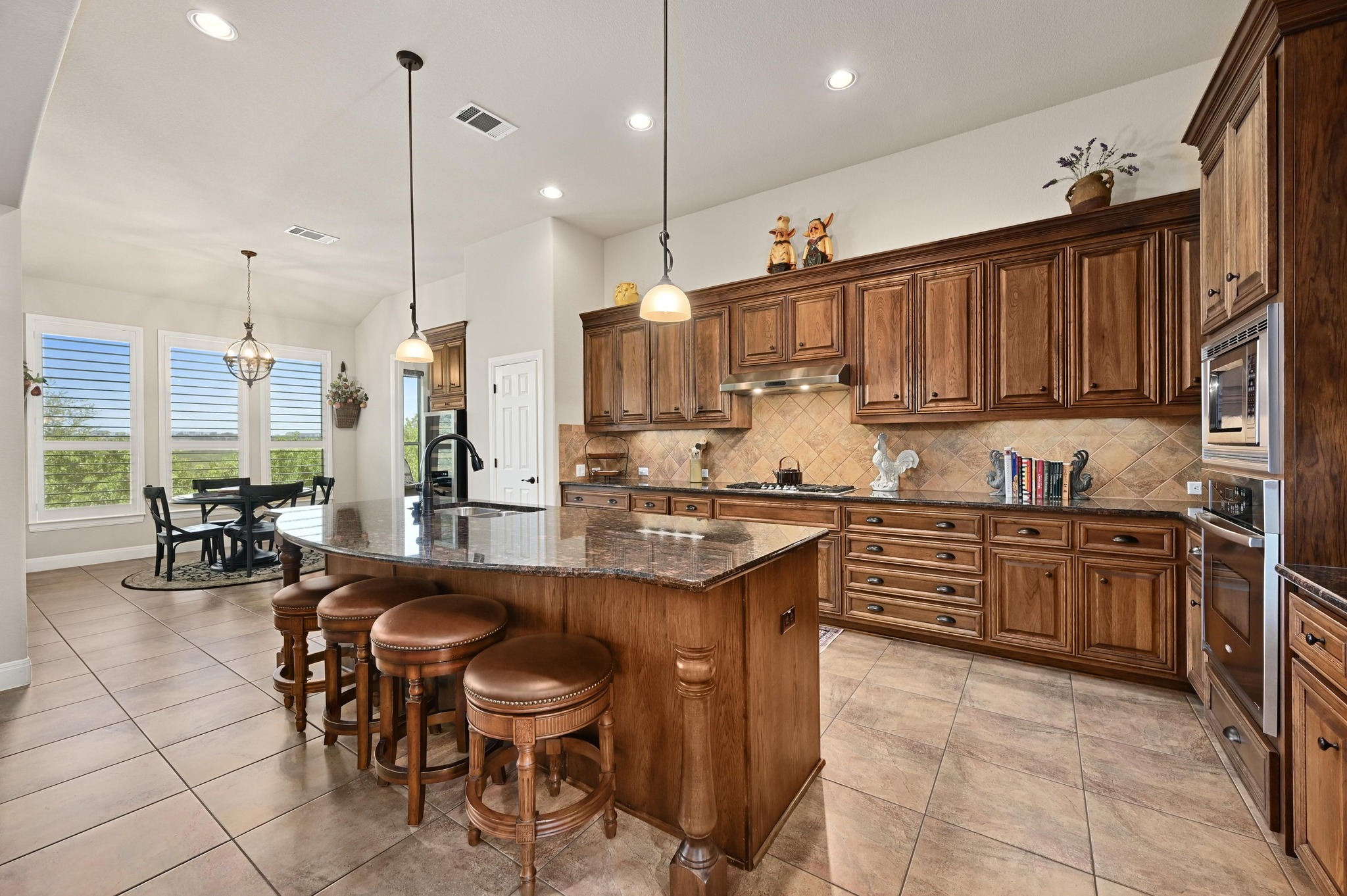 16129 Zagros Way Austin, TX 78738 - Photo 10 of 25 Kitchen featuring granite counters, a kitchen breakfast bar, wood finish cabinets, an island with sink, and stainless steel appliances