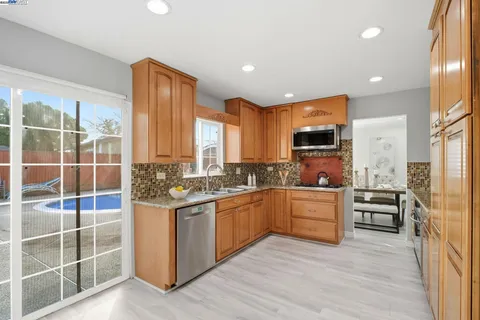 a kitchen with stainless steel appliances granite countertop a stove top oven a refrigerator a sink and dishwasher with wooden floor