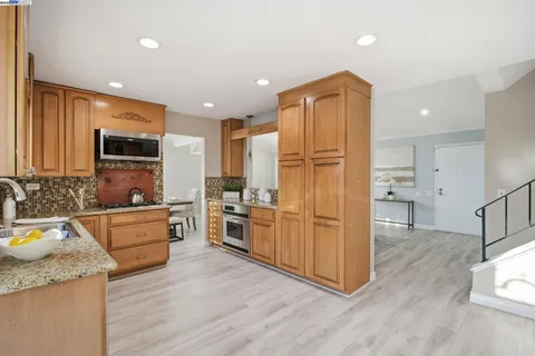 a kitchen with stainless steel appliances granite countertop a refrigerator a stove top oven a sink dishwasher and wooden cabinets with wooden floor