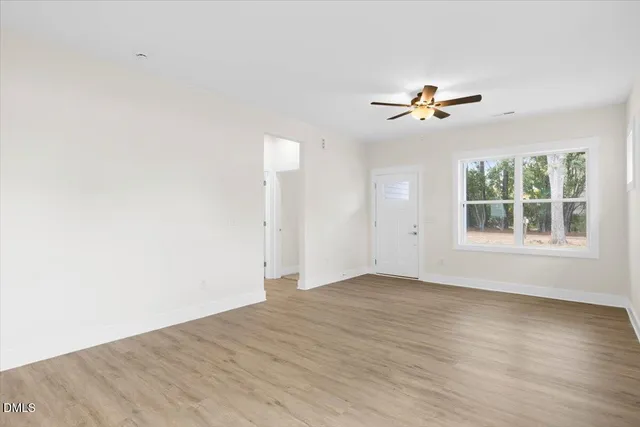 an empty room with wooden floor chandelier fan and windows