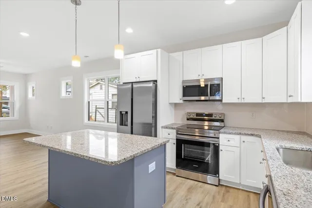 a kitchen with stainless steel appliances granite countertop a stove a refrigerator a sink a microwave oven with white cabinets and wooden floor