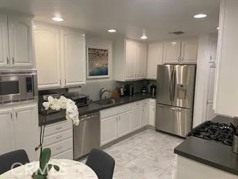 a kitchen with granite countertop a refrigerator a stove a microwave and white cabinets