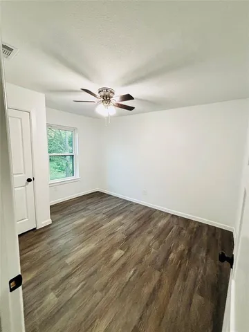 an empty room with wooden floor chandelier fan and windows