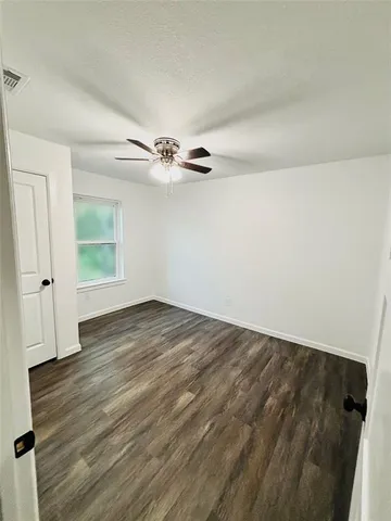 an empty room with wooden floor chandelier fan and windows