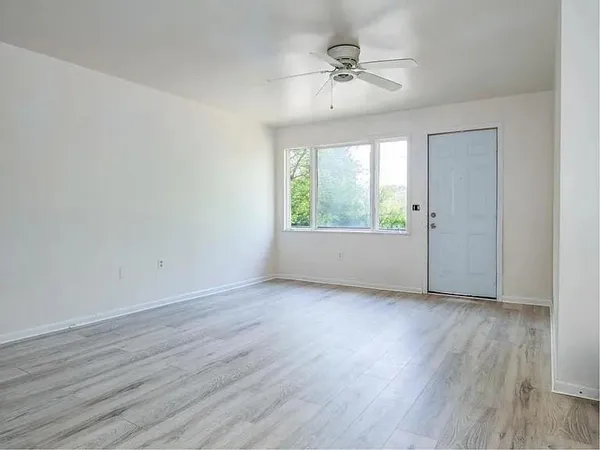 an empty room with wooden floor fan and windows