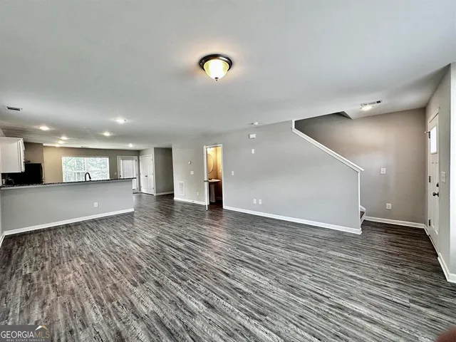a view of an empty room with wooden floor and a kitchen