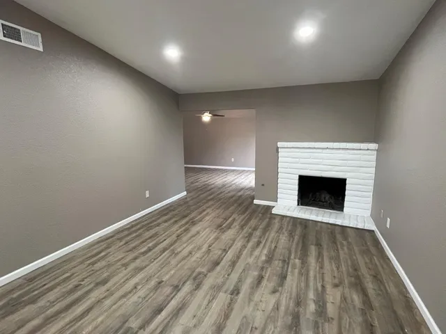 a view of an empty room with wooden floor a fireplace and a window