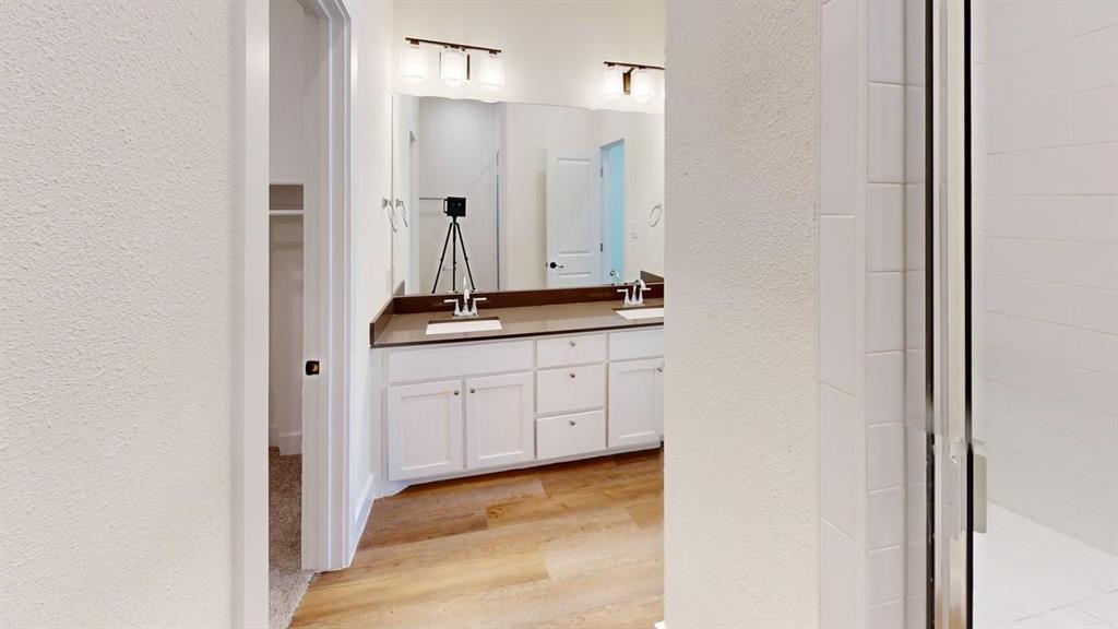 353 Buck Ridge Drive Little Elm, TX 75068 - Photo 18 of 23 Bathroom featuring a textured wall, double vanity, light wood finished floors, a shower stall, and a spacious closet