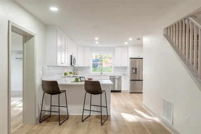 a kitchen with stainless steel appliances kitchen island granite countertop a stove a refrigerator and white cabinets with wooden floor