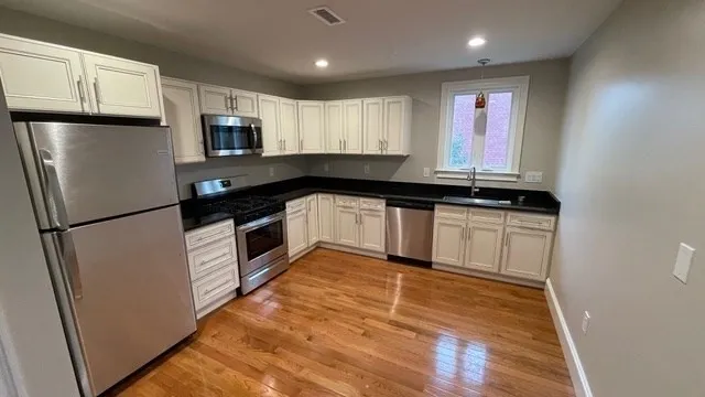 a kitchen with granite countertop a refrigerator a sink and white cabinets