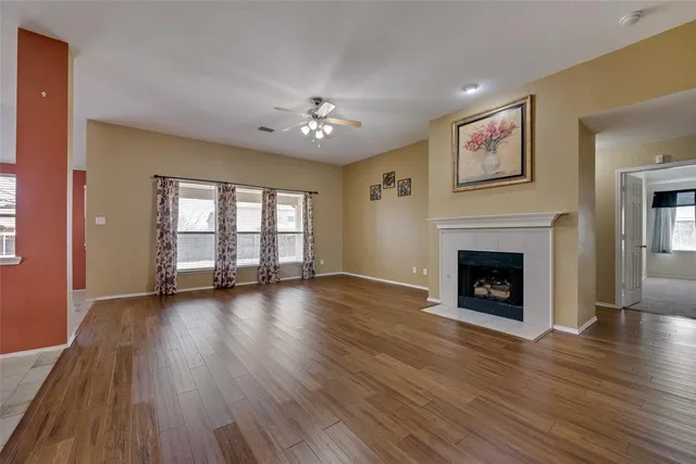 a view of an empty room with wooden floor fireplace and a window