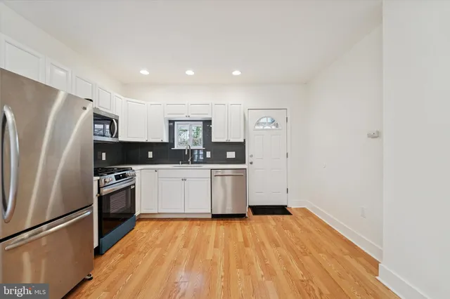 a kitchen with granite countertop a refrigerator oven a sink dishwasher and white cabinets with wooden floor