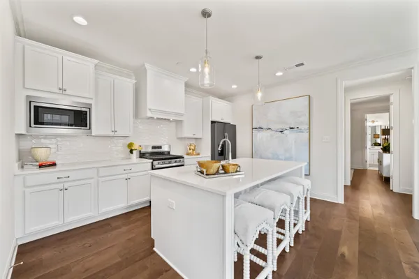 a kitchen with stainless steel appliances granite countertop a sink a stove a refrigerator and white cabinets with wooden floor