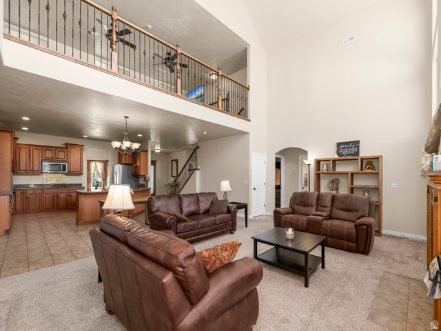 255 East 1200 North Mapleton, UT 84664 - Photo 4 of 37 Vaulted living space featuring an upper-level balcony with wrought iron spindles, a visible kitchen with wood cabinetry and tile flooring, and a carpeted living area