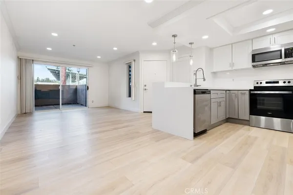 a large white kitchen with stainless steel appliances kitchen island granite countertop a stove a sink a refrigerator and white cabinets with wooden floor