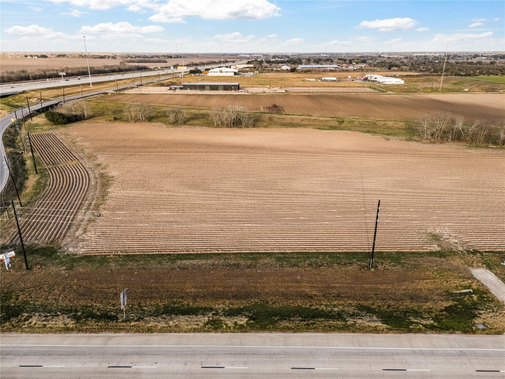 0 Hartledge Road Rosenberg, TX 77471 - Photo 5 of 13 This photo shows a large, flat agricultural field with neatly plowed rows, bordered by a main road. The area is open and expansive, with some industrial buildings in the distance under a clear blue sky.