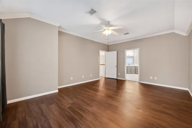 a view of an empty room with wooden floor and a ceiling fan