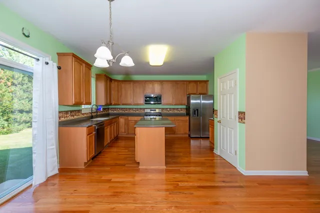 a kitchen with stainless steel appliances granite countertop a refrigerator a sink dishwasher a stove and white cabinets with wooden floor