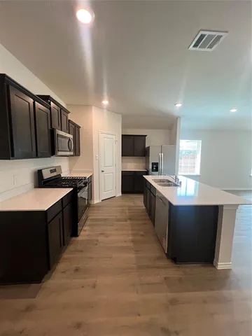 a large kitchen with stainless steel appliances kitchen island granite countertop a stove a sink dishwasher and a refrigerator with wooden floor