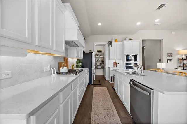 a large kitchen with stainless steel appliances kitchen island a large counter top a stove a chimney a sink and a refrigerator