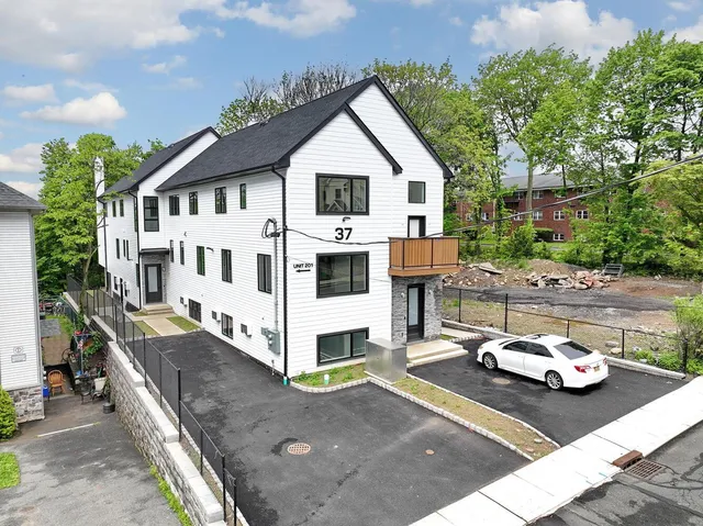 a view of a white house with a small yard and large trees
