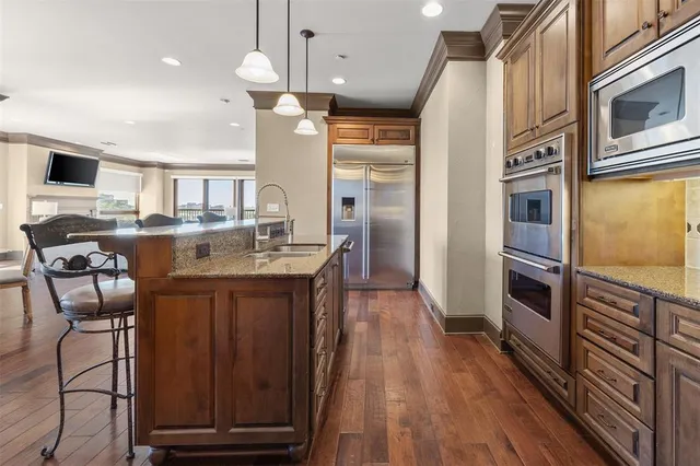 a kitchen with stainless steel appliances granite countertop a refrigerator a stove top oven a sink dishwasher and wooden cabinets with wooden floor