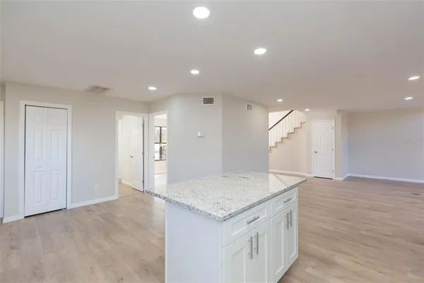 a large kitchen with stainless steel appliances granite countertop a stove a sink a refrigerator and white cabinets with wooden floor