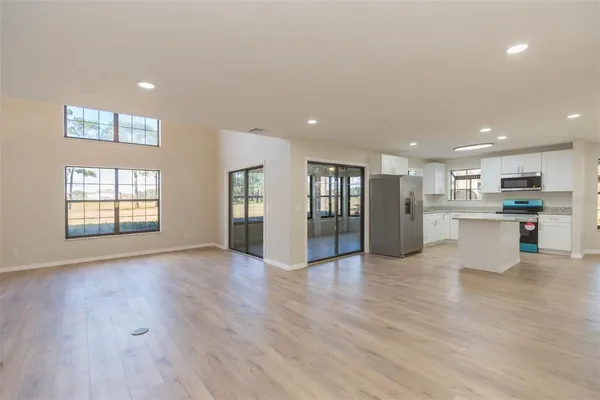 a view of an empty room with wooden floor and a kitchen
