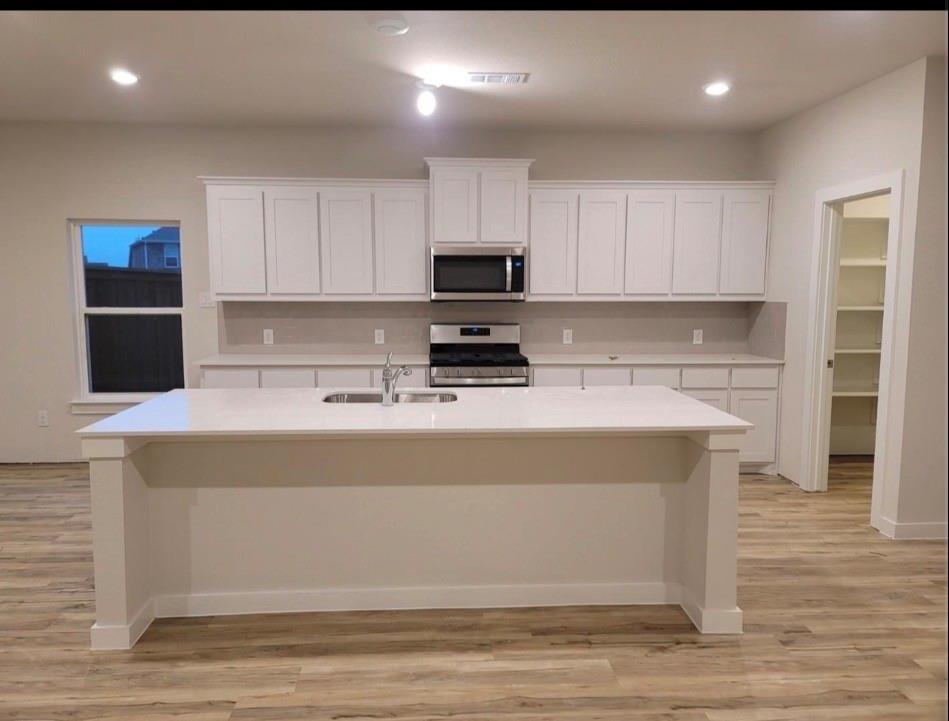 785 Vineyard Way Forney, TX 75126 - Photo 4 of 12 Spacious kitchen featuring white cabinetry, a large island with an integrated sink, stainless steel appliances, and wood-look flooring