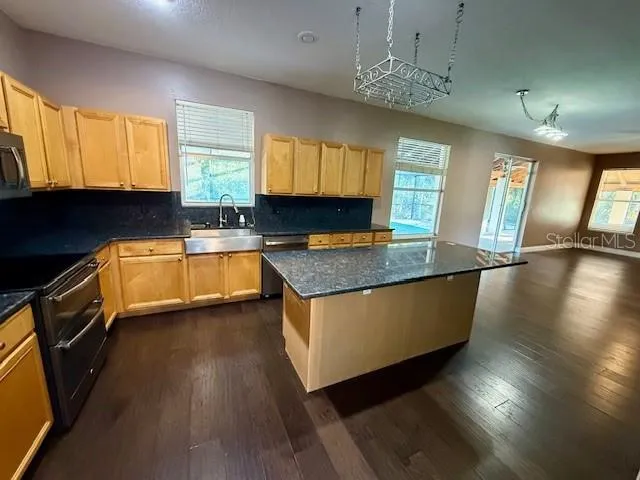 a kitchen with granite countertop a stove a sink a refrigerator wooden floor and cabinets