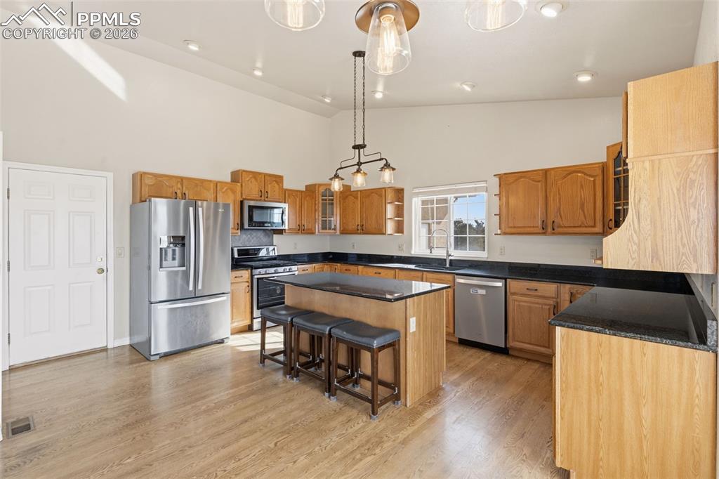11515 Texarkanna Road Peyton, CO 80831 - Photo 16 of 43 Kitchen with glass insert cabinets, stainless steel appliances, a center island, vaulted ceiling, and a breakfast bar