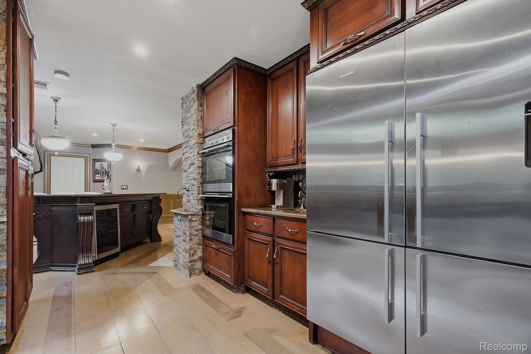 1258 Priscilla Lane Rochester, MI 48309 - Photo 24 of 56 Kitchen area featuring a built-in stainless steel refrigerator, double wall ovens, wood-finish flooring, cherry-stained cabinetry, and decorative stone column accents