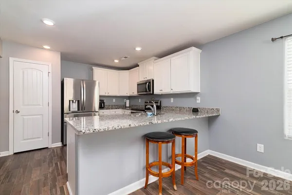 a kitchen with stainless steel appliances granite countertop a stove a sink a refrigerator white cabinets and a refrigerator with wooden floor