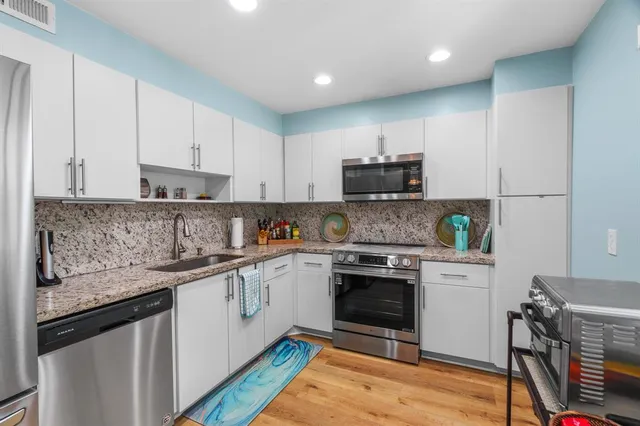 a kitchen with granite countertop a stove top oven a sink dishwasher and a refrigerator with wooden floor