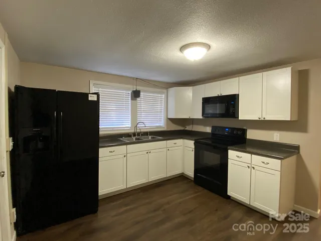 a kitchen with granite countertop white cabinets a refrigerator and a sink