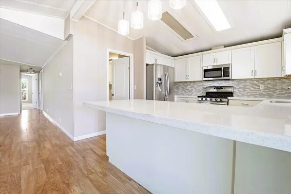 a kitchen with stainless steel appliances granite countertop a refrigerator a sink a stove and white cabinets with wooden floor