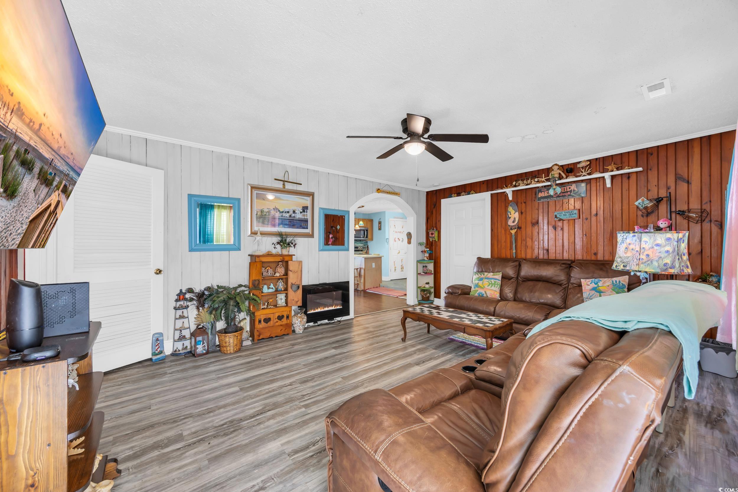 1616 Perrin Drive North Myrtle Beach, SC 29582 - Photo 3 of 40 Living room featuring ornamental molding, a ceiling fan, a glass covered fireplace, arched walkways, and wood walls