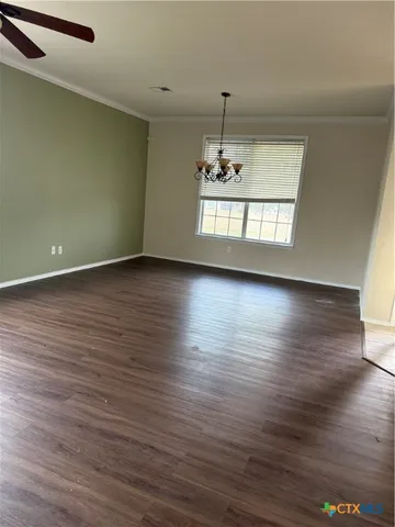 an empty room with wooden floor chandelier and windows