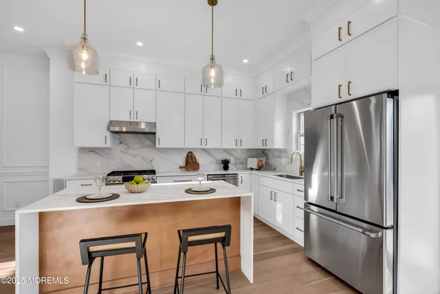 a kitchen with stainless steel appliances granite countertop a refrigerator a sink dishwasher a stove and white cabinets with wooden floor