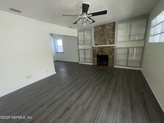 an empty room with wooden floor fireplace and windows