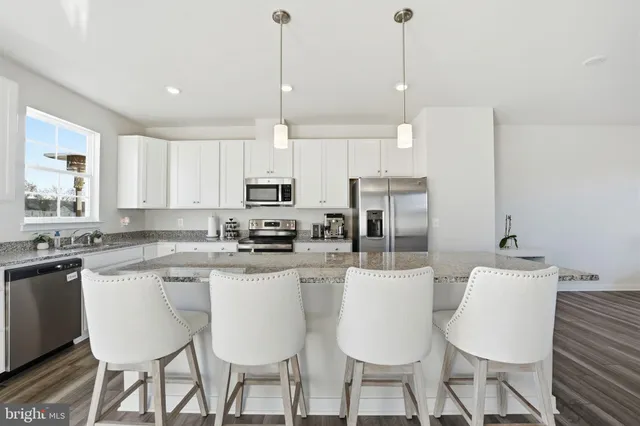 a kitchen with stainless steel appliances kitchen island granite countertop a dining table chairs and white cabinets