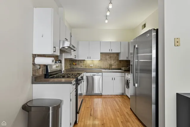 a kitchen with stainless steel appliances granite countertop a refrigerator a stove and a sink with wooden floor