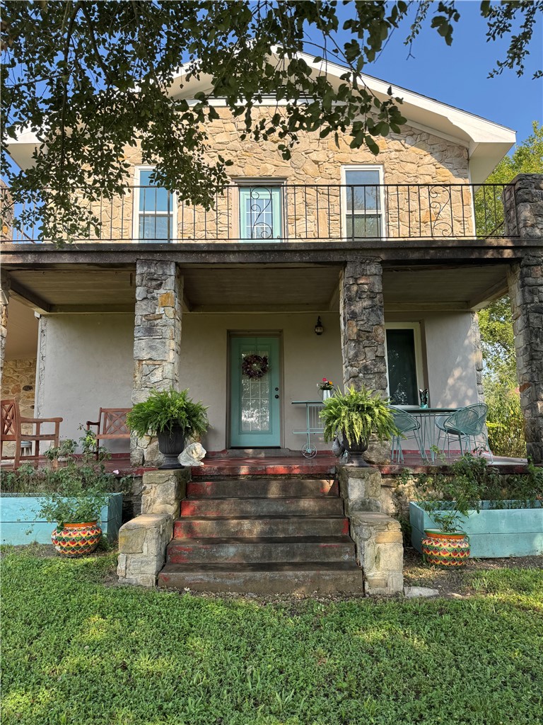 Back of property with stone siding, stucco siding, and a porch