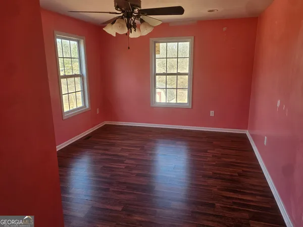 an empty room with wooden floor chandelier fan and windows